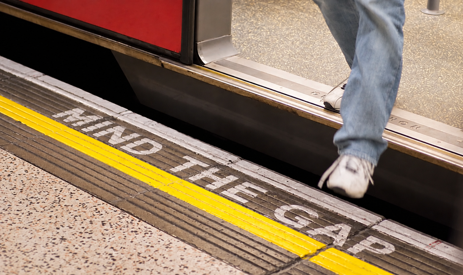 Person in light blue jeans stepping across a subway platform gap beside a “MIND THE GAP” warning, illustrating the distance between a brand’s claimed purpose and the evidence consumers can verify.